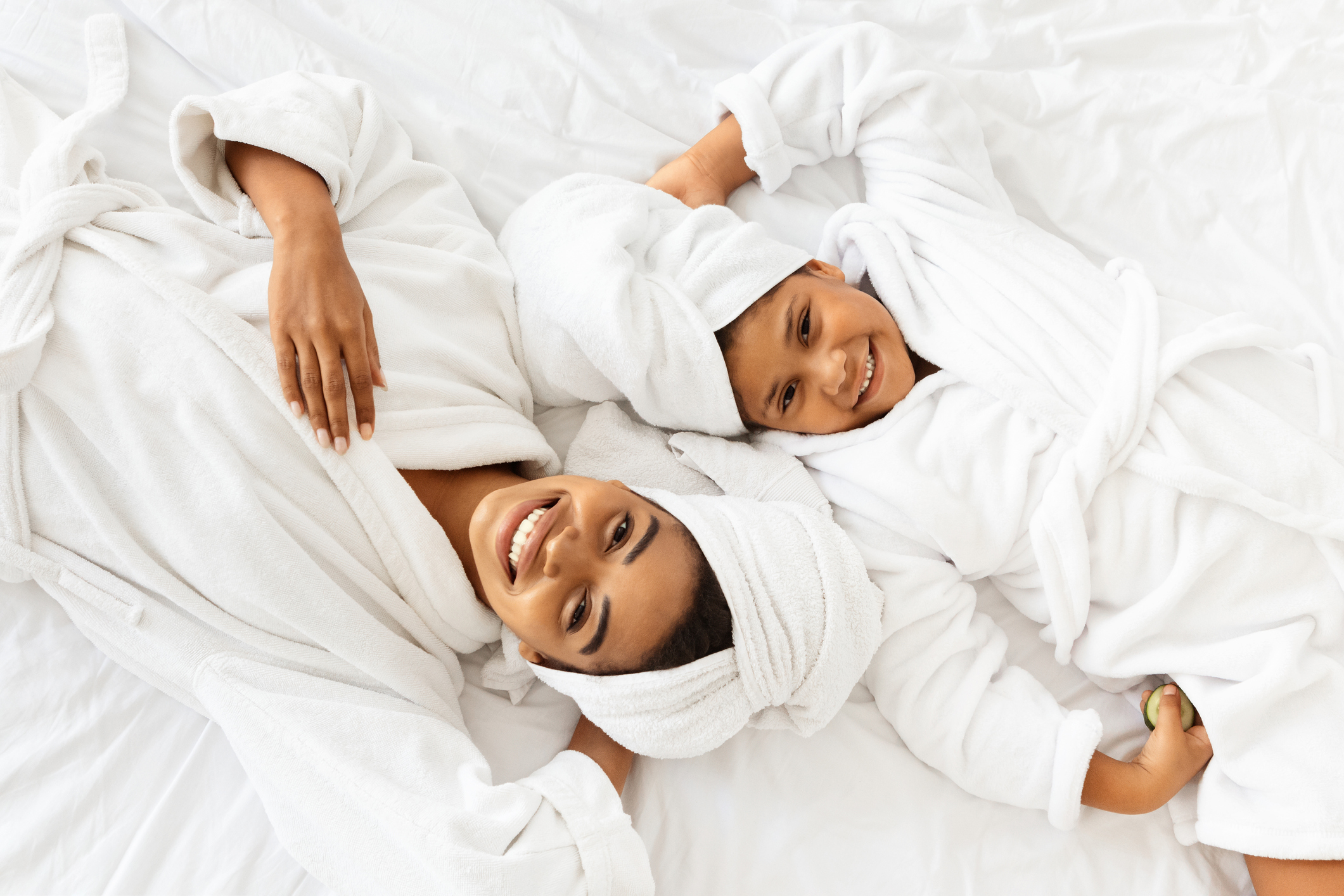 Happy African Mother And Daughter In Bathrobes And Towels Lying On Bed